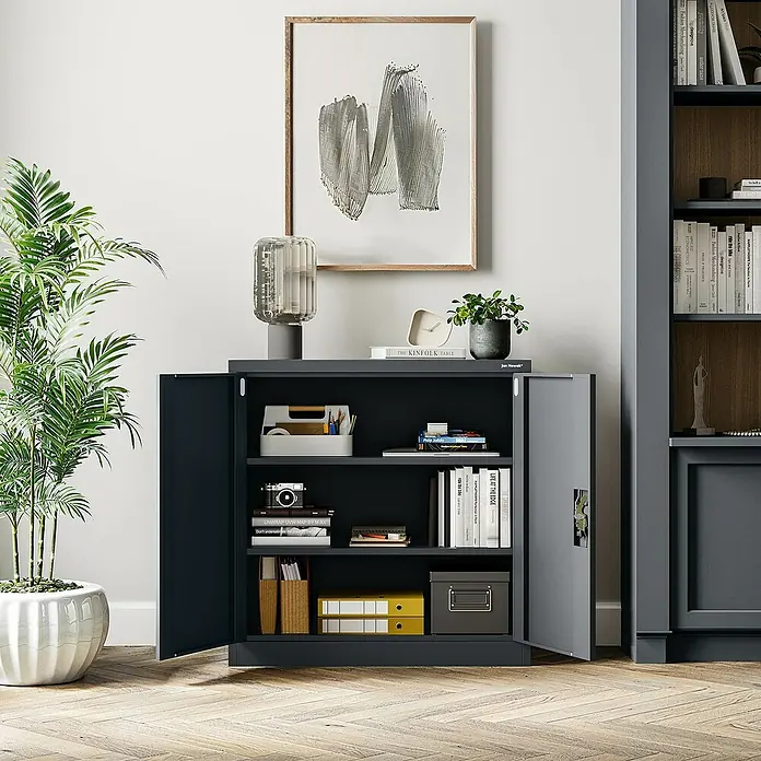 Jan Nowak Aktenschrank Beata - B x T x H: 90 x 40 x 92,5 cm, Anthrazit - Ein grauer Aktenschrank mit geöffneten Türen, gefüllt mit Büchern und Büromaterial, unter einem modernen Gemälde.