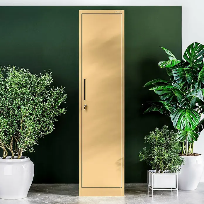 Jan Nowak Aktenschrank Alex - B x T x H: 45 x 40 x 185 cm, Beige - Ein schlanker, sandfarbener Spind mit einer einzigen Tür und minimalistischem Design, umgeben von üppigen Pflanzen.