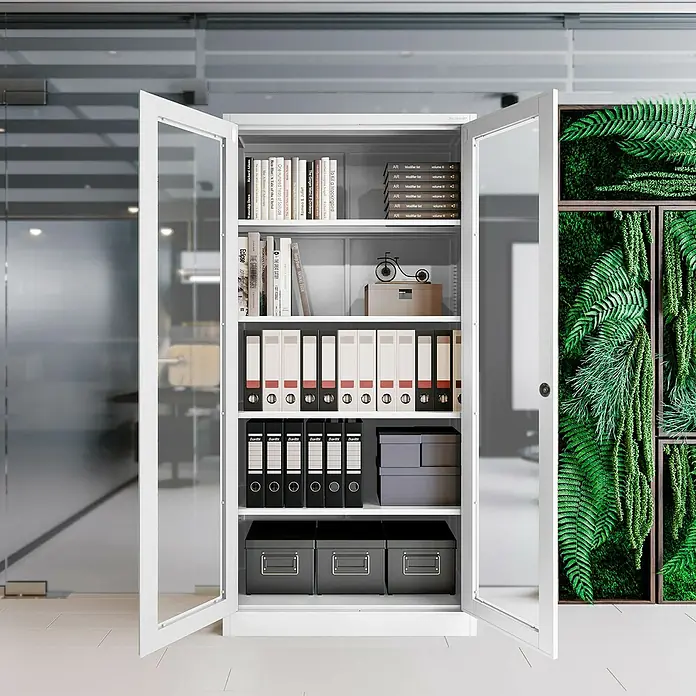 Jan Nowak Aktenschrank Amelia - B x T x H: 90 x 40 x 185 cm, Weiß - Büroschrank mit Glastüren, gefüllt mit Ordnern, Büchern und Boxen, vor Bürohintergrund.