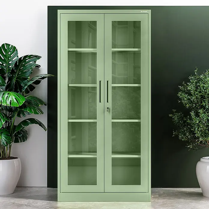 Jan Nowak Aktenschrank Amelia - B x T x H: 90 x 40 x 185 cm, Grün - Ein grüner Stahlschrank mit Glastüren und Regalen steht zwischen zwei Zimmerpflanzen. Der Schrank ist hellgrün und verfügt über abschließbare Türen.