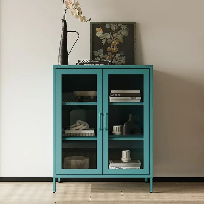 Jan Nowak Vitrine Gina - B x T x H: 80 x 40 x 101,5 cm, Meeresgrün - Eine blaue Vitrine mit Glasböden steht vor einer weißen Wand und zeigt dekorative Gegenstände und Bücher.