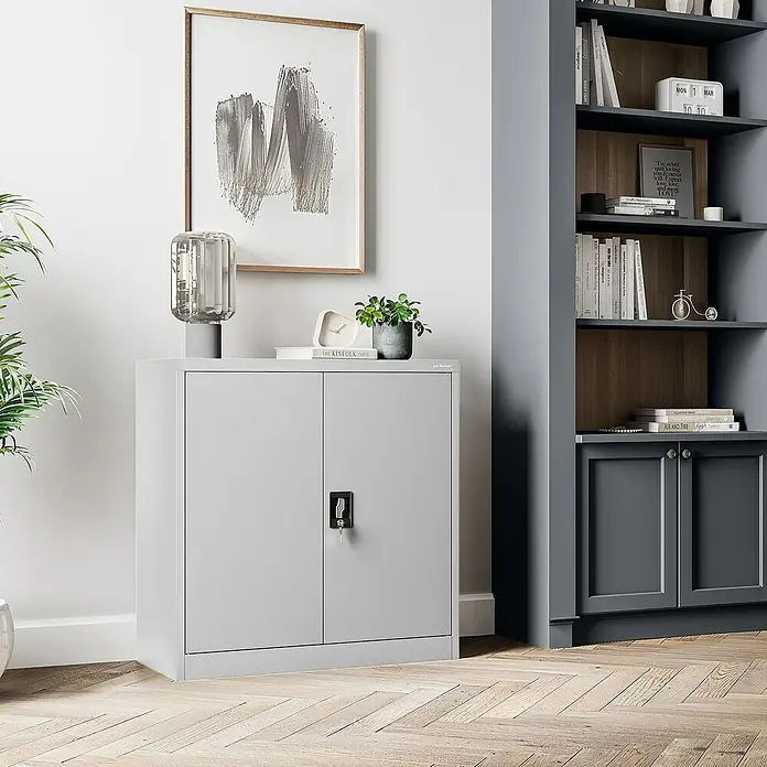 Jan Nowak Aktenschrank Beata - B x T x H: 90 x 40 x 92,5 cm, Grau - Hier ist ein grauer Büroschrank mit zwei Türen. Auf der Oberseite des Schranks stehen dekorative Gegenstände und ein Bild hängt an der Wand.