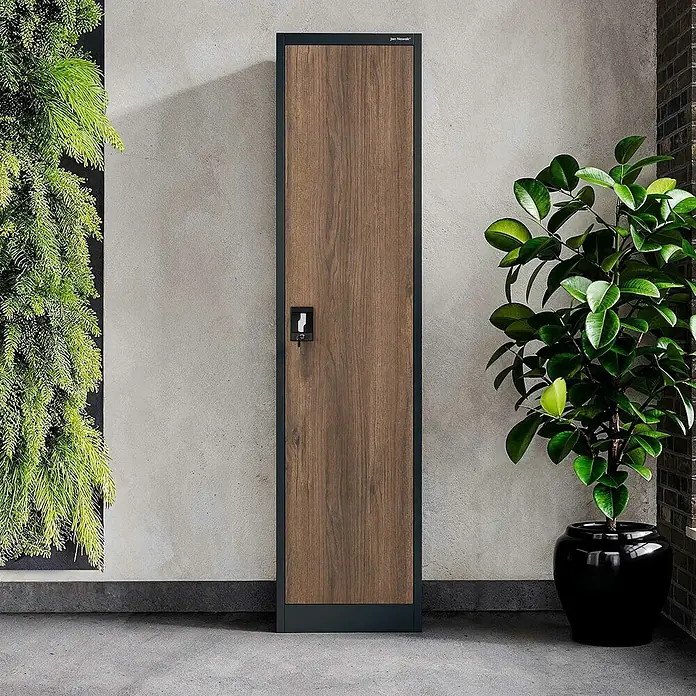 Jan Nowak Aktenschrank Alex - B x T x H: 45 x 40 x 185 cm, Anthrazit/ Nussbaum - Aufnahme eines Spindschranks mit Holzfront und schwarzem Rahmen, der neben Pflanzen steht.