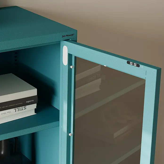 Jan Nowak Vitrine Gina - B x T x H: 80 x 40 x 101,5 cm, Meeresgrün - Nahaufnahme eines blauen Metallschranks mit Glasfront und Büchern im Inneren. Das Produkt ist ein moderner und stilvoller Schrank.