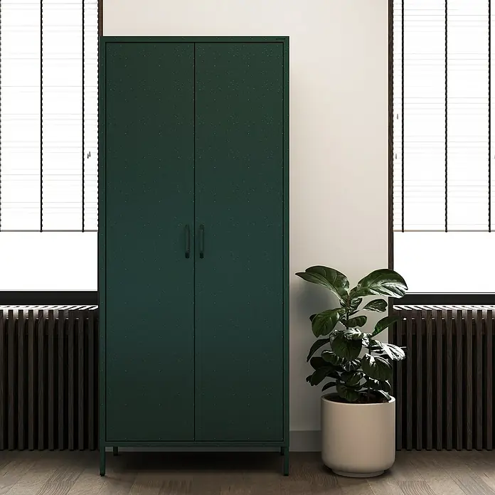 Jan Nowak Kleiderschrank Flavio - H x B x T: 185 x 80 x 45 cm, Flaschengrün - Schrank im Interieur. Der grüne Schrank steht vor einer Wand zwischen einem Fenster und einem Topf mit einer Pflanze.