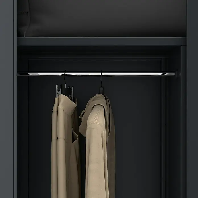 Jan Nowak Metall-Mehrzweckschrank Dawid - H x B x T: 185 x 90 x 45 cm, Anthrazit - Nahaufnahme von Kleidungsstücken an einer Kleiderstange in einem dunklen Kleiderschrank, der durch eine LED-Leuchte beleuchtet wird.