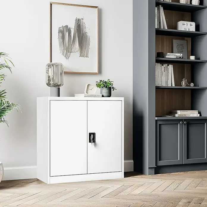 Jan Nowak Aktenschrank Beata - B x T x H: 90 x 40 x 92,5 cm, Weiß - Ein weißer Aktenschrank mit zwei Türen und Schloss steht in einem stilvollen Raum mit Parkettboden und einem passenden Bücherregal.