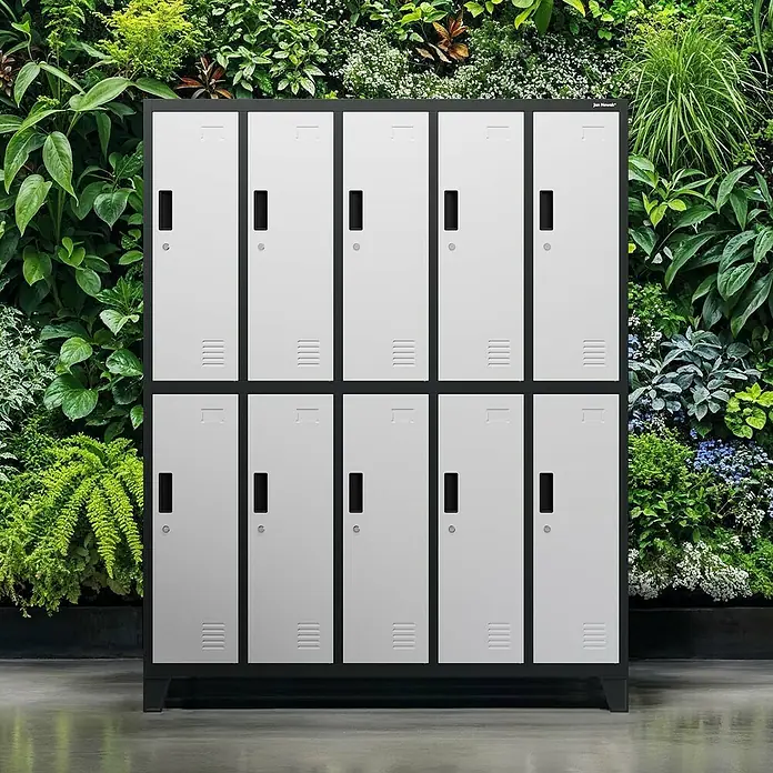 Jan Nowak Spind Bartek - B x T x H: 136 x 45 x 172 cm, Anthrazit / Weiß - Schrank mit 10 Fächern in grau-weiß vor einem grünen Pflanzenwand. Das Metallmöbelstück bietet Stauraum und fügt sich in die grüne Umgebung ein.