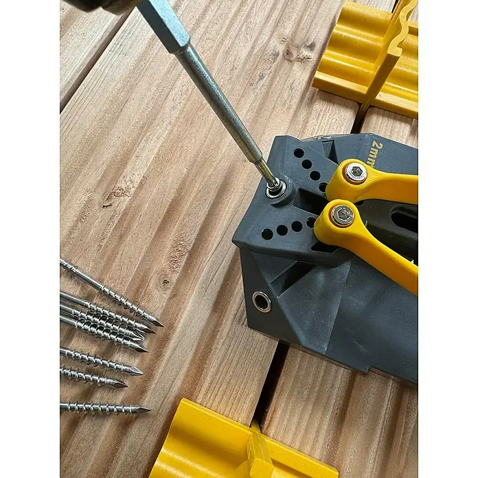 Fast Tornillo para terraza - Ø x L: 4,8 x 60 mm, 200 ud. - Primer plano de un destornillador atornillando un tornillo en una plantilla de terraza gris sobre un suelo de madera, mostrando la herramienta.