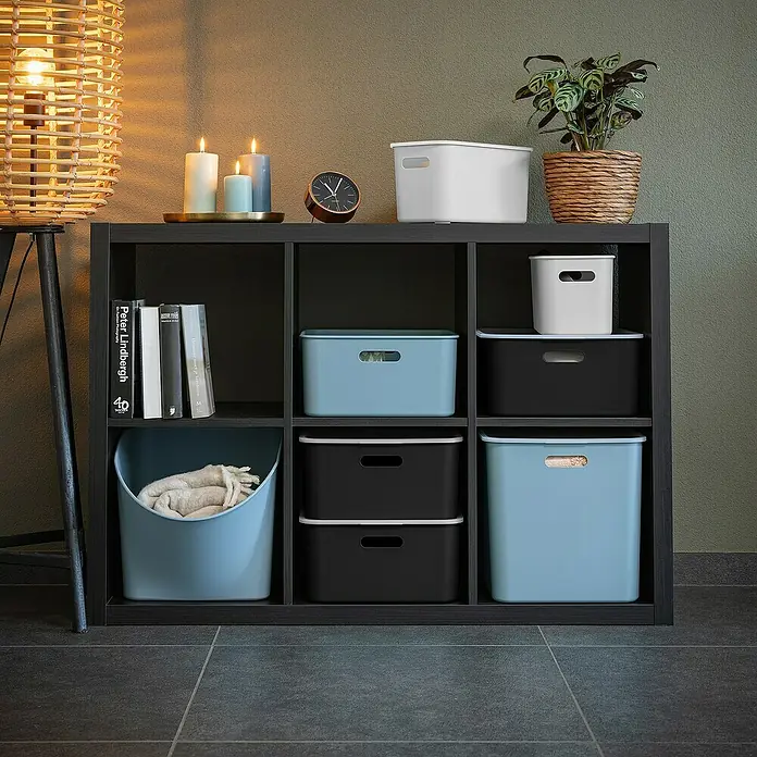 Sunware Sigma home Aufbewahrungsbox cube box - L x B x H: 31 x 31 x 31 cm, Kunststoff, Blau, 25 l - Bücherregal mit blauen, weißen und schwarzen Aufbewahrungsboxen, einem Korb, Büchern, Kerzen und einer Uhr, neben einer Stehlampe und einer Pflanze.