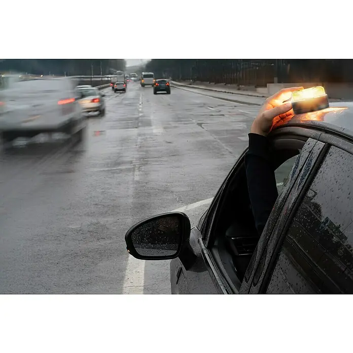 Luz de emergencia V16 Conectada NK - Apto para: Avería en el vehículo, Transmisión de datos: Red móvil - Una mano está fijando una luz de advertencia amarilla en el techo de un coche negro con tiempo lluvioso para indicar una avería.