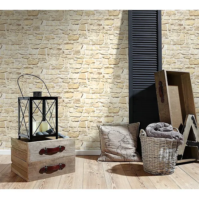 A.S. Création Il Decoro Vliestapete Steine - Beige, Steinoptik, 10,05 x 0,53 m - Einrichtungsidee mit rustikalem Charme: Laterne auf Holzkisten, Kissen und Korb vor einer Steinwand für ein gemütliches Ambiente.