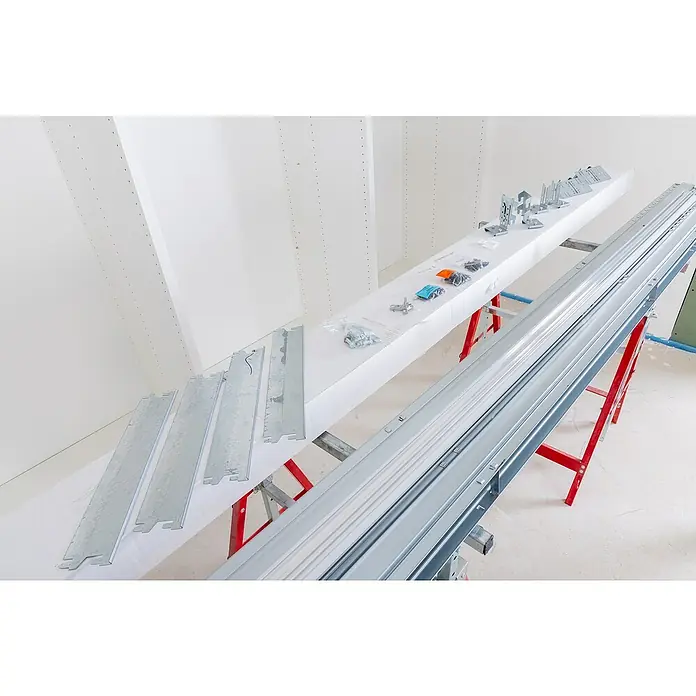 Knauf Pocket Kit Easy Schiebetürsystem Standard - Stahl, Für CW 75 mm - Montagefertige Möbelteile auf einer Werkbank, darunter Metallstreben, Beschläge und eine lange Führungsschiene für den Zusammenbau.