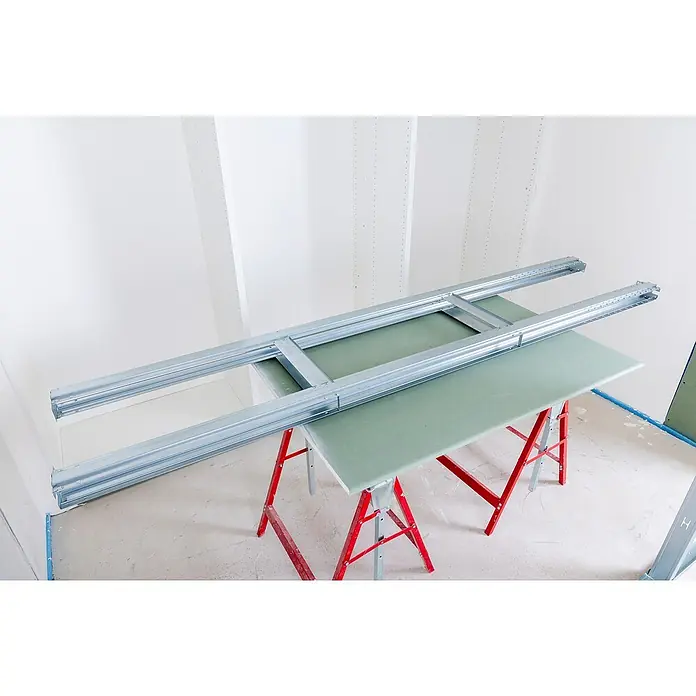 Knauf Pocket Kit Easy Schiebetürsystem Standard - Stahl, Für CW 75 mm - Nahaufnahme des Metallrahmens auf dem Tisch mit Gipskartonplatte, der für die Installation im Raum bereit ist.