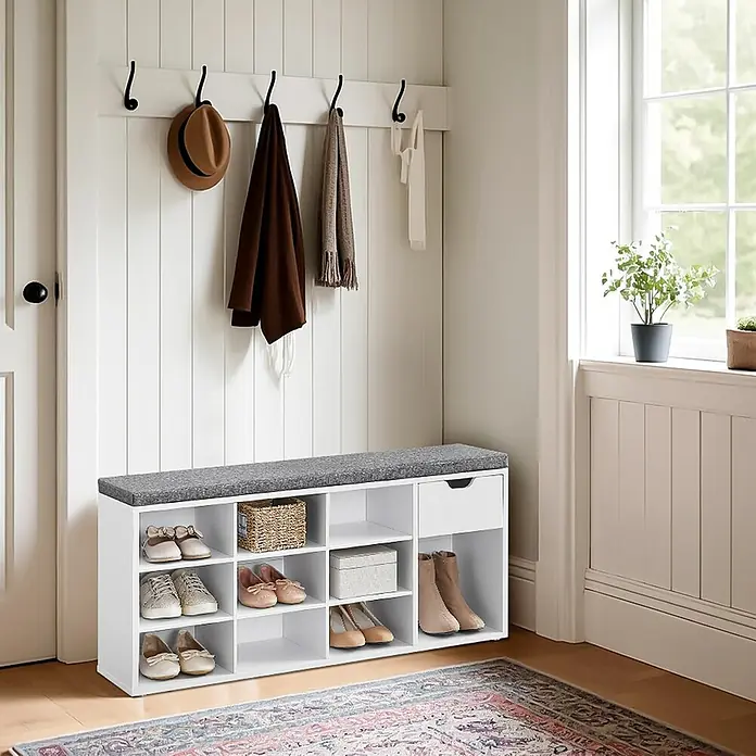 Schuhbank mit Schublade - 30 x 104 x 48 cm, Weiß/Grau - Ein weißer Schuhschrank mit grauem Sitzkissen und Hakenleiste an einer weißen Wand mit Tür und Fenster. Der Schuhschrank bietet viel Stauraum.