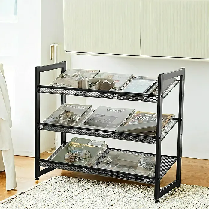 Schuhregal - L x B x H: 30,7 x 74 x 62,8 cm, Schwarz - Ein dreistöckiges, schwarzes Metallregal ist mit Zeitschriften, Kopfhörern und einem Tablet gefüllt. Das Regal steht auf einem beigen Teppich vor einer Wand.
