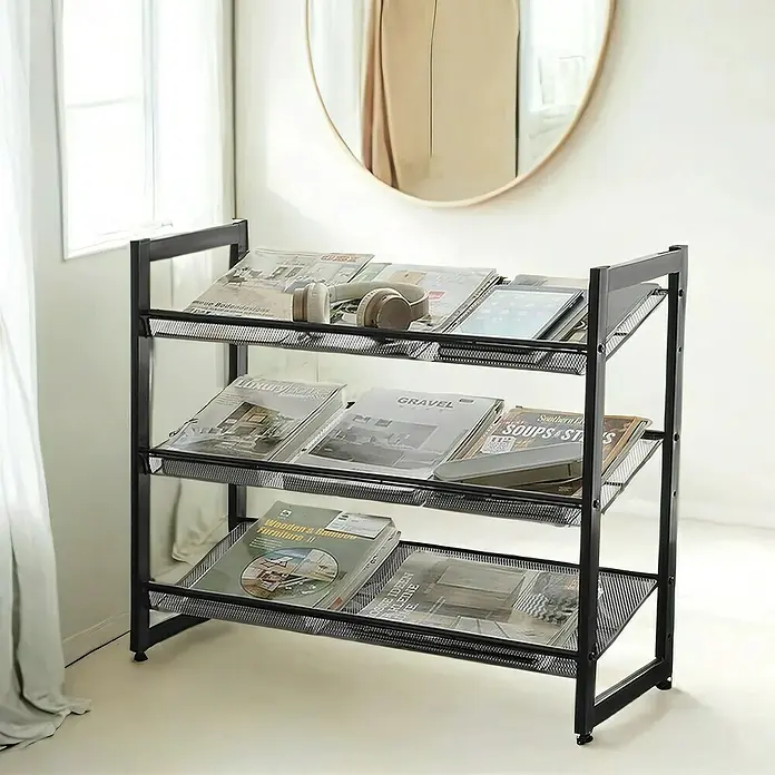 Schuhregal - L x B x H: 30,7 x 74 x 62,8 cm, Schwarz - Schwarzes Zeitschriftenregal mit drei Ablagen, gefüllt mit Zeitschriften und Accessoires, vor einer hellen Wand und einem runden Spiegel.