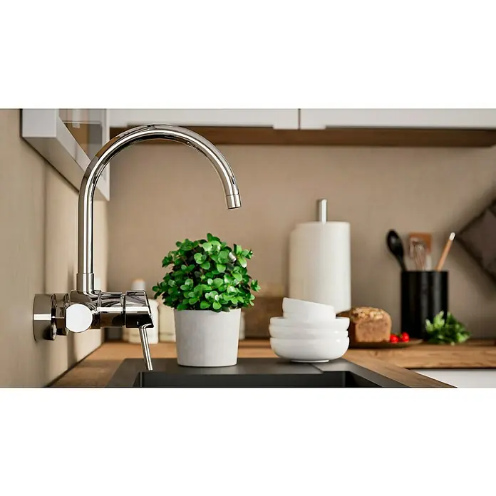 Grohe Concetto Spültischarmatur - Chrom, Glänzend, Wandmontage - Nahaufnahme eines glänzenden Küchenwasserhahns mit einer kleinen Pflanze im Vordergrund.