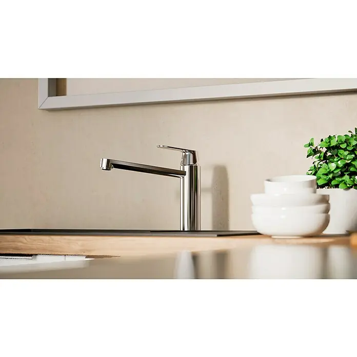 Grohe Eurosmart Cosmopolitan Spültischarmatur - L-Auslauf, Chrom, Glänzend, Schwenkbar - Elegante Chrom Küchenarmatur vor hellem Hintergrund. Der Wasserhahn ist modern gestaltet und harmoniert mit den weißen Schalen und der Pflanze.