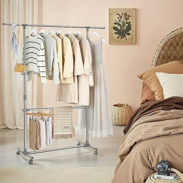 Kleiderwagen - Länge: 49 cm, Höhenverstellung: 115 cm - 180 cm, Grau - Kleiderständer mit Kleidung und Accessoires in einem hellen Schlafzimmer. Der Kleiderständer ist aus Metall und hat zwei Stangen.