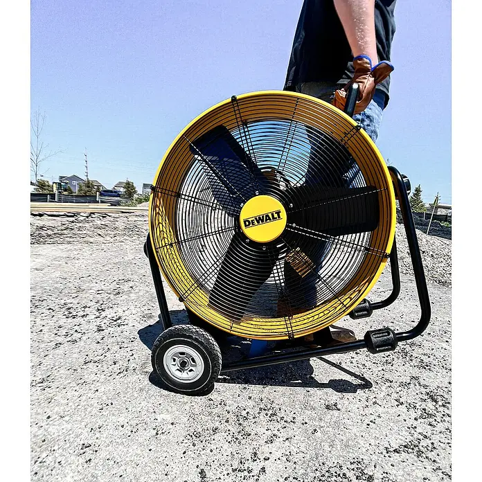 DeWalt Bodenventilator DXF2410 - 190 W, Max. Luftleistung: 148,77 m³/h - Ein gelber DeWalt-Ventilator mit schwarzen Rotorblättern, der auf einer Baustelle steht und von einer Person gehalten wird.