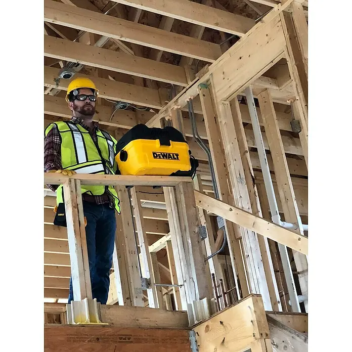 DeWalt Elektro-Nass- & Trockensauger DXV15T - 1.100 W, Behältervolumen: 15 l, Filterreinigung: Vollautomatisch - Ein Bauarbeiter mit einem gelben DeWalt Staubsauger auf einer Baustelle, mit Fokus auf dem Werkzeug und der Arbeitsumgebung.