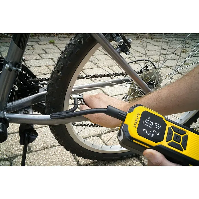 DeWalt Akku-Luftpumpe SXIF0101 - 11,1 V, 10 bar, Füllleistung: 14,2 l/min - Nahaufnahme einer Person, die einen Fahrradreifen mit einer gelben STANLEY-Luftpumpe aufpumpt. Die digitale Anzeige zeigt den Reifendruck.