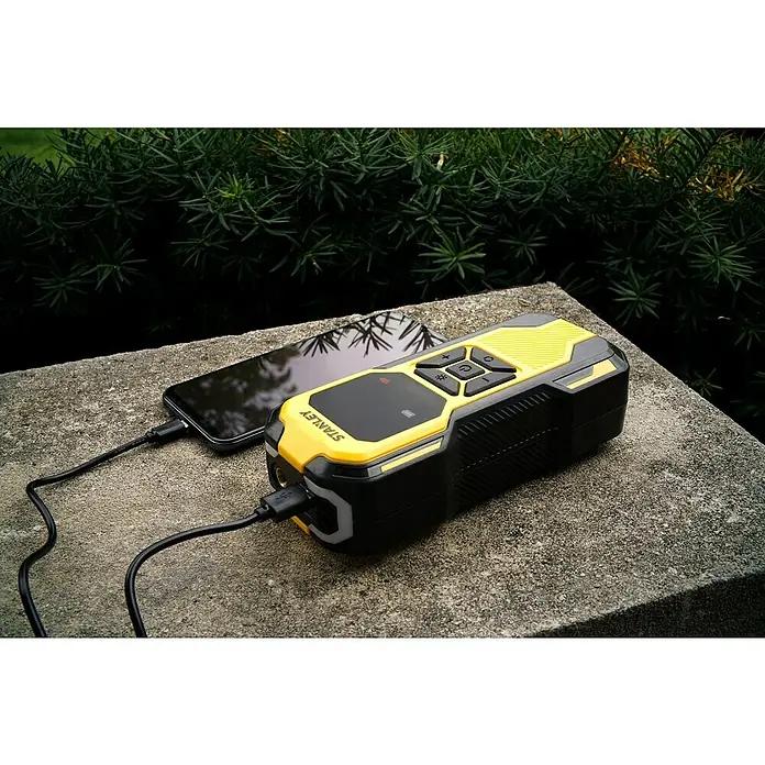 DeWalt Akku-Luftpumpe SXIF0101 - 11,1 V, 10 bar, Füllleistung: 14,2 l/min - Das Bild zeigt einen Stanley-Batterieladegerät in Schwarz und Gelb, das ein Smartphone auflädt. Das Gerät liegt auf einer Steinoberfläche.