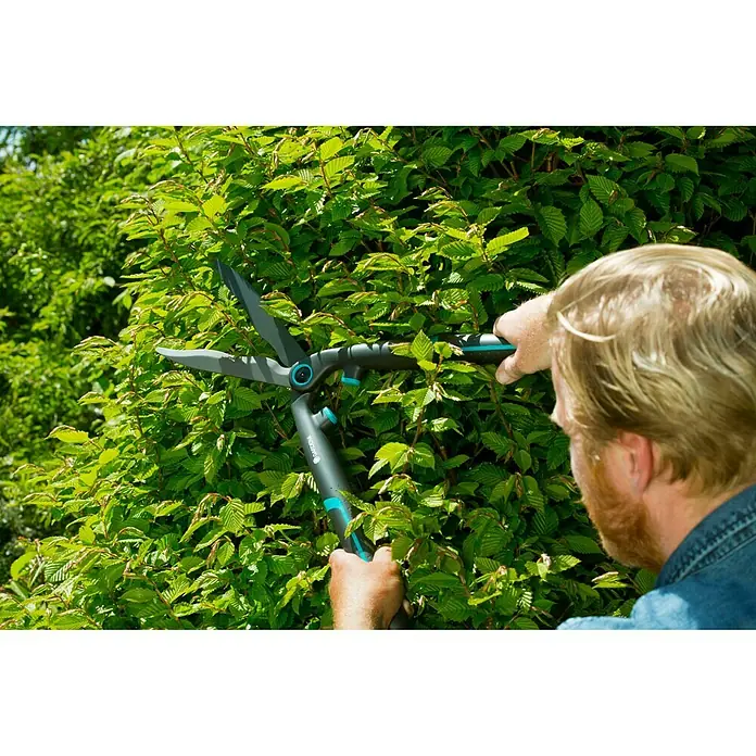 Gardena EasyCut Tijeras de podar manuales - Largo: 640 mm - Primer plano de una persona que utiliza tijeras cortasetos Gardena para recortar un denso seto verde, destacando la herramienta.