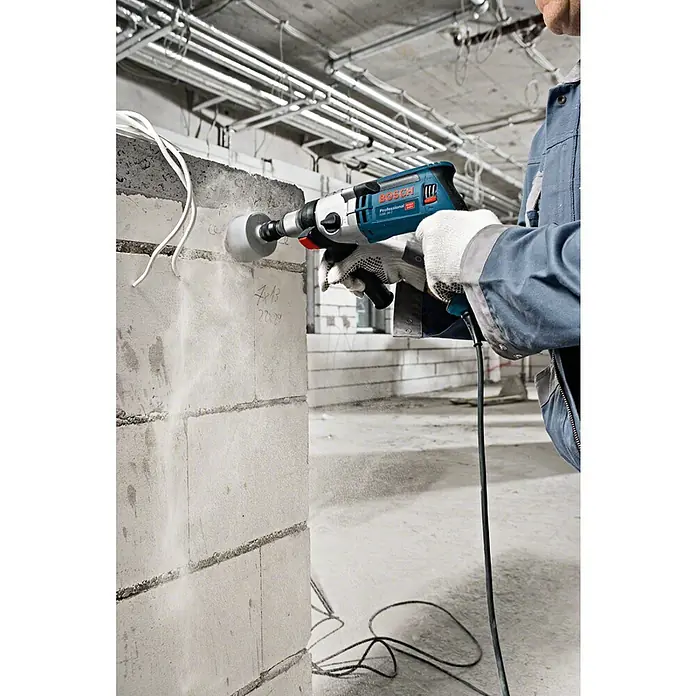 Bosch Professional Schlagbohrmaschine GSB 24-2 - 1.100 W, Schnellspannbohrfutter - Ein Handwerker bohrt mit einer blauen Bosch Professional Bohrmaschine ein Loch in eine Wand. Staub wirbelt um den Bohrer.