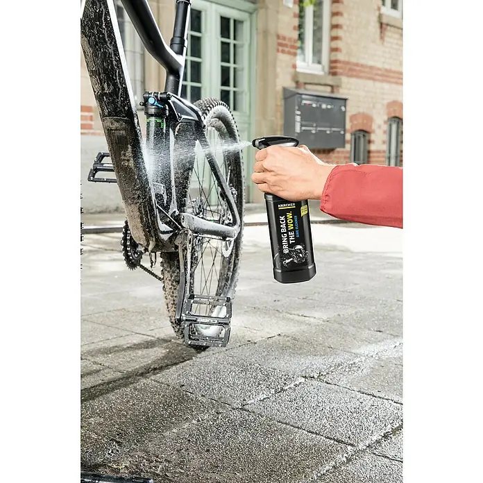 Kärcher Zweirad-Reiniger - 500 ml - Ein Mann sprüht Kärcher Fahrradreiniger auf ein schmutziges Fahrrad, um es zu reinigen. Die Flasche des Reinigers ist gut sichtbar im Bild.