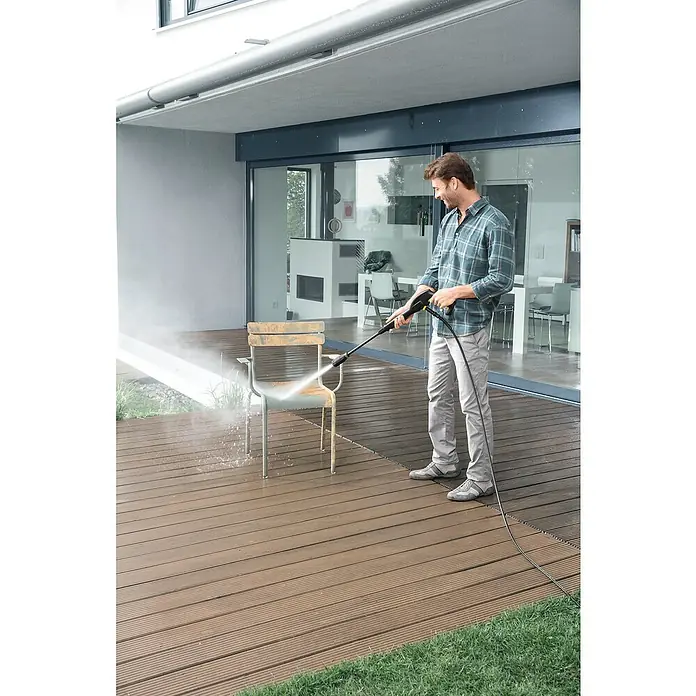 Kärcher Universalreiniger RM 555 - 5 l - Ein Mann reinigt einen Stuhl mit einem Hochdruckreiniger auf einer Terrasse. Der Reiniger sprüht Wasser auf den Stuhl, um Schmutz zu entfernen.