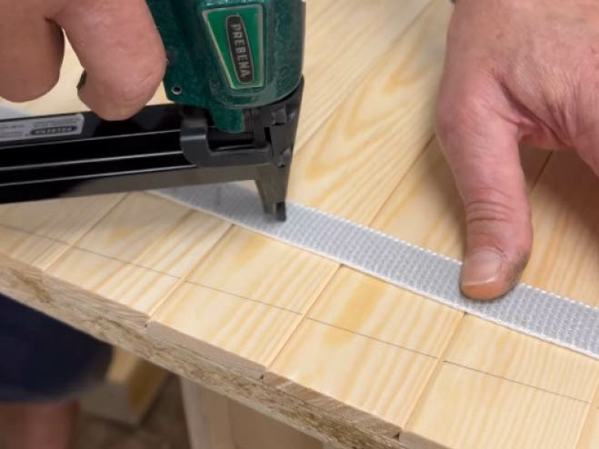 Mit einem Drucklufttacker wird ein Klettband auf Holzlatten getackert