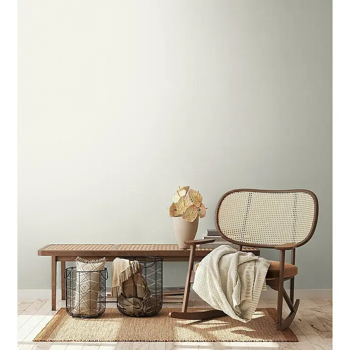 A.S. Création Aquarell Dreams Vliestapete - Weiß, Uni, 10,05 x 0,53 m - Ein gemütliches Interieur mit einem Rattan-Schaukelstuhl, einer Bank, Körben und einem Teppich, die eine warme und einladende Atmosphäre schaffen.