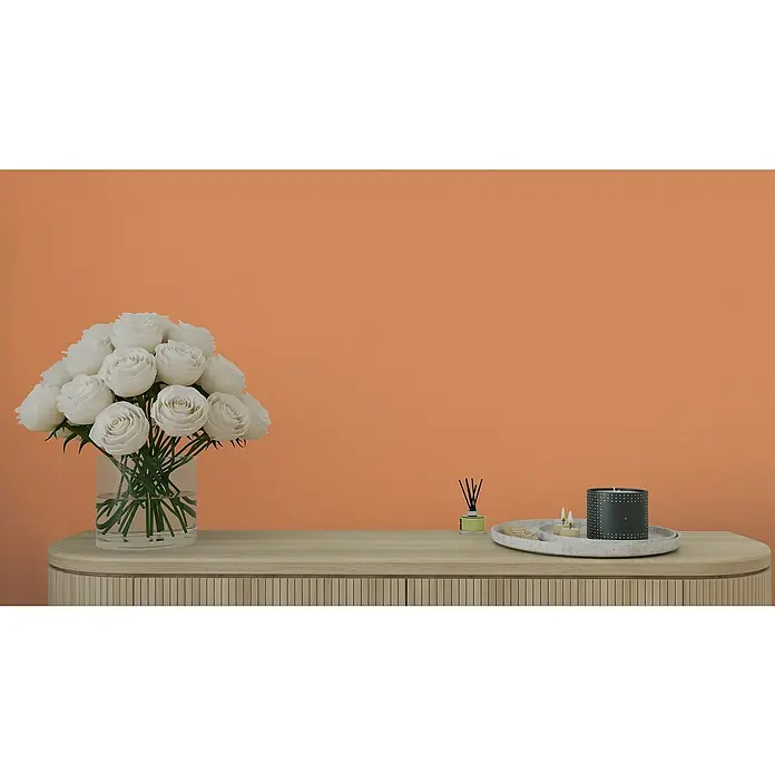A.S. Création Aquarell Dreams Vliestapete - Orange, Uni, 10,05 x 0,53 m - Stillleben mit weißen Rosen in einer Vase, Duftstäbchen und Kerze auf einem Sideboard vor orangefarbenem Hintergrund.