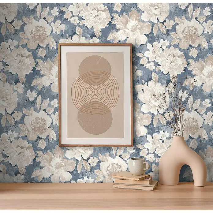 A.S. Création Aquarell Dreams Vliestapete - Blau-Beige, Floral, 10,05 x 0,53 m - Ein gerahmtes Kunstwerk mit abstrakten Kreisen hängt an einer blauen floralen Wand, ergänzt durch eine skulpturale Vase und Bücher auf einem Holztisch.