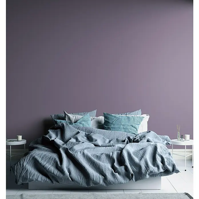A.S. Création Aquarell Dreams Vliestapete - Lila, Uni, 10,05 x 0,53 m - Schlafzimmer mit großem Bett, blauer Bettwäsche und Nachttischen vor einer lila Wand.