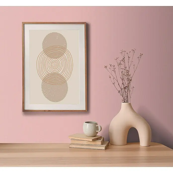 A.S. Création Aquarell Dreams Vliestapete - Rosa, Uni, 10,05 x 0,53 m - Ein gerahmtes, abstraktes Kunstwerk mit Kreisen und neutralen Farben hängt über einem Tisch mit Deko-Objekten.