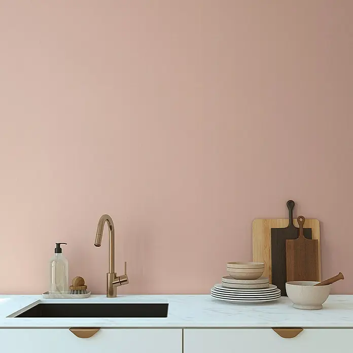 A.S. Création Aquarell Dreams Vliestapete - Apricot-Rosa, Uni, 10,05 x 0,53 m - Detailansicht einer Küche mit einer eleganten Armatur, Geschirr und Schneidebrettern vor einer rosafarbenen Wand.