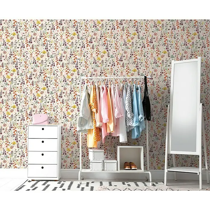 A.S. Création Aquarell Dreams Vliestapete - Beige-Bunt, Floral, 10,05 x 0,53 m - Ein stilvolles Zimmer mit einer weißen Kommode, einer Kleiderstange mit bunten Kleidungsstücken und einem großen Spiegel vor einer floralen Tapete.
