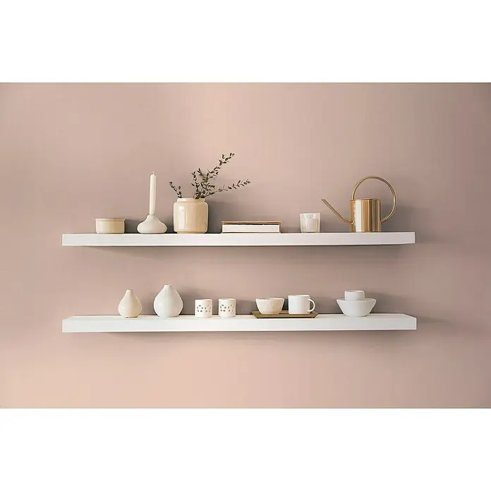 A.S. Création Aquarell Dreams Vliestapete - Apricot-Rosa, Uni, 10,05 x 0,53 m - Zwei schwebende weiße Regale an einer rosa Wand mit dekorativen Artikeln wie Kerzen, Vasen und einer goldenen Gießkanne.