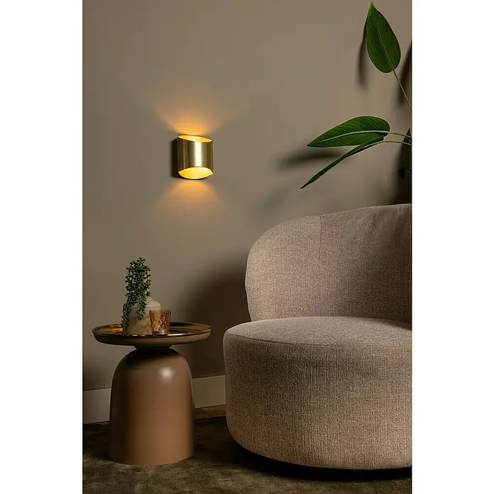 Lucide Wandleuchte Diletta - 40 W, L x B x H: 22,5 x 16 x 8,5 cm, Gold, G9 - Wandleuchte aus gebürstetem Gold beleuchtet elegant eine Wand neben einem beigen Sessel und einem runden Beistelltisch.