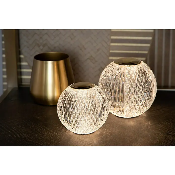 Lucide Cintra Tischleuchte rund - 1,5 W, Ø x H: 9 x 10 cm, Kristall - Zwei leuchtende Kristallkugellampen und ein goldener Übertopf auf einem dunklen Tisch.