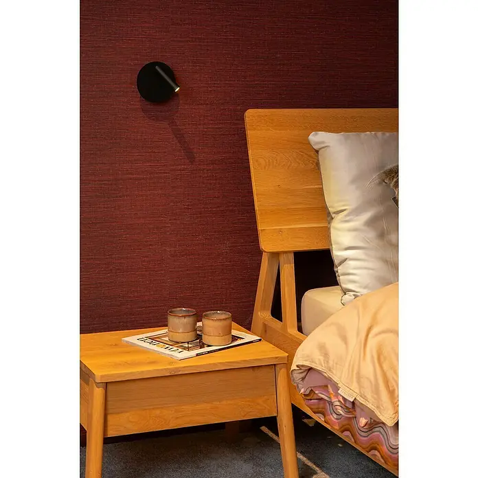 Lucide Akku-Wandleuchte Jolijn - 12 x 12 x 9 cm, Schwarz, Neutralweiß, 2 W, IP20 - Gemütliches Schlafzimmerambiente mit Nachttischlampe, zwei Keramikbechern und einem Holzbett vor einer strukturierten roten Wand.