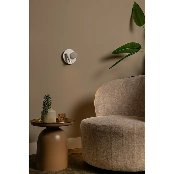 Lucide LED-Wandleuchte rund Matiz - 3,5 W, Ø x H: 16,5 x 19 cm, Weiß, Neutralweiß - Seitenansicht eines Raumes mit einem beigen Sessel, einem Beistelltisch und einer modernen weißen Wandleuchte.