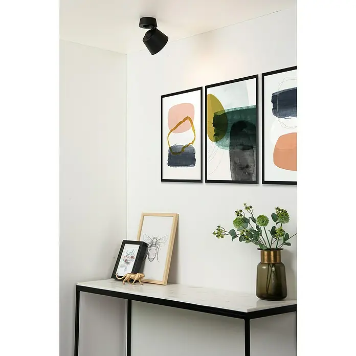 Lucide Deckenstrahler Trigono - 40 W, L x B x H: 11 x 11 x 11 cm, Schwarz, GU10, Anzahl Leuchtmittel: 1 Stk. - Eine moderne Raumansicht mit stilvollen Wandbildern und einer eleganten Tischdekoration unter einem schwarzen Deckenstrahler.