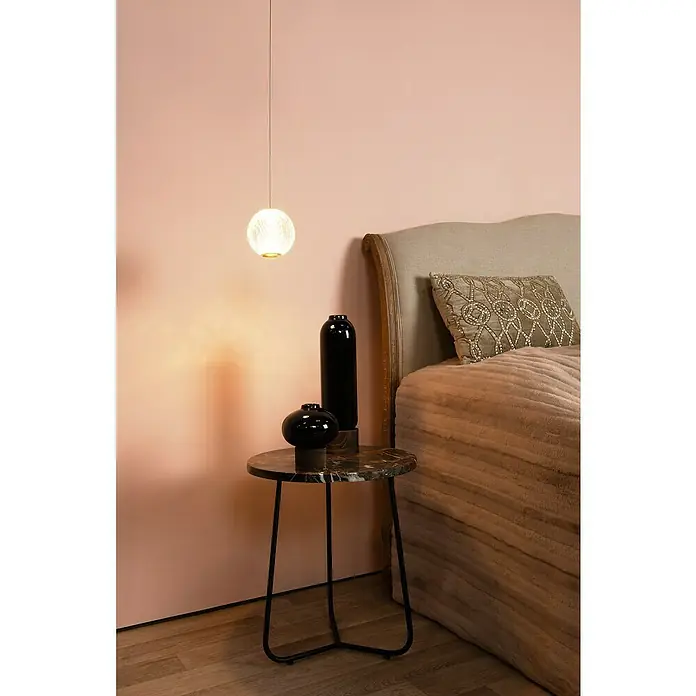 Lucide Cintra LED-Pendelleuchte rund - 5,7 W, L x B x H: 150 x 14 x 14 cm, Kristall, Anzahl Leuchtmittel: 1 Stk. - Elegante Szene mit einer modernen Pendelleuchte über einem Marmortisch mit schwarzen Vasen, neben einem stilvollen Bett.