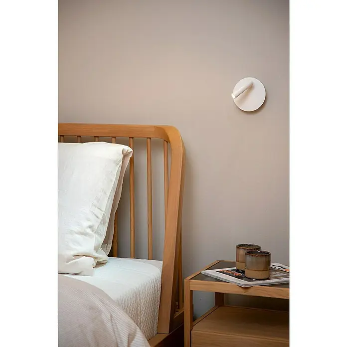Lucide Akku-Wandleuchte Jolijn - 12 x 12 x 9 cm, Weiß, Neutralweiß, 2 W, IP20 - Nahaufnahme eines Schlafzimmers mit einem Holzbett und einer Nachttischlampe mit zwei Tassen auf einem Nachttisch.