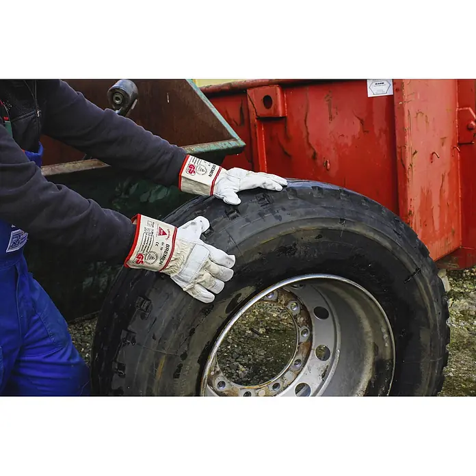 Hase Safety Arbeitshandschuhe Bremen - Handschuhgröße: 10, Weiß - Nahaufnahme einer Person, die mit Bremen-Arbeitshandschuhen einen LKW-Reifen berührt, vor dem Hintergrund eines Containers.