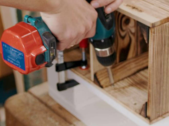 Eine Holzkiste wird an der Unterseite einer weißen Palette angeschraubt